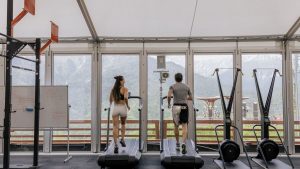 Two people running on treadmills in a gym with scenic mountain views.